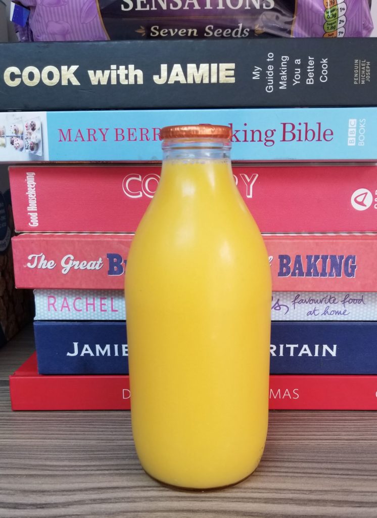 Orange juice in a glass bottle in front of cookbookes