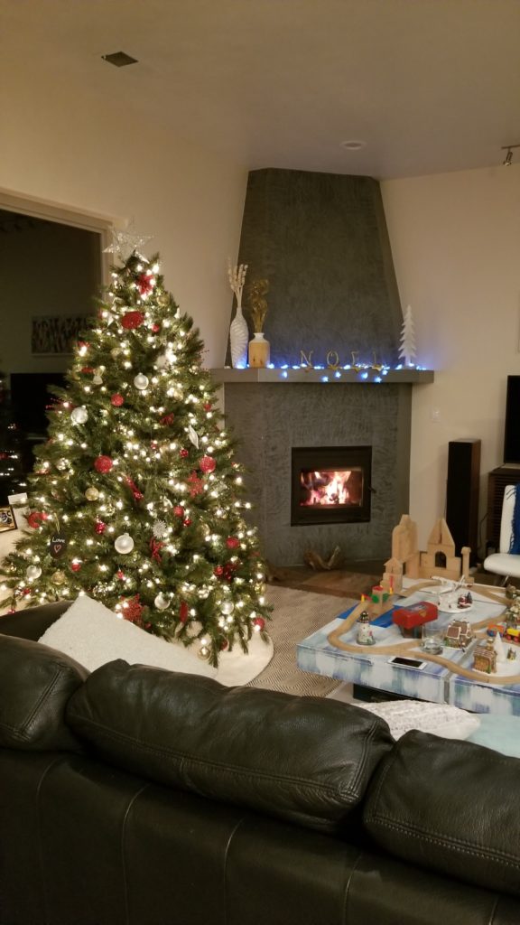 Christmas Tree standing next to a fire place.